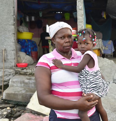 Tessa, a mother of 10, stands in front of her ruined house in Haiti holding her daughter in her arms Photo: Fabienne Douce/ActionAid.