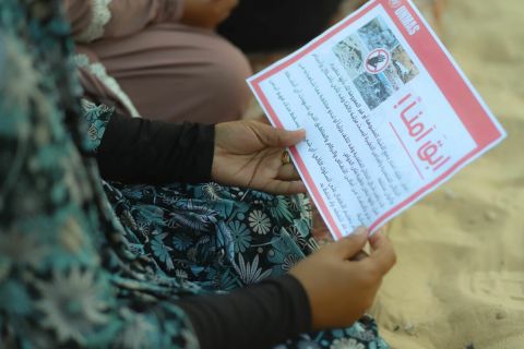 A hand holding a leaflet in Arabic